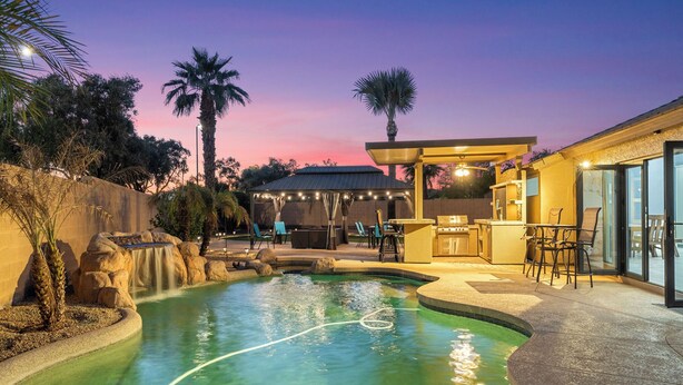A swimming pool with a waterfall feature, surrounded by palm trees and a patio area with outdoor seating. - Swim, Golf, Grill & Chill! Surprise Group Getaway (Surprise)