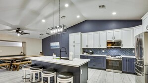 A modern kitchen with a large island, dark blue cabinets, and stainless steel appliances. - Swim, Golf, Grill & Chill! Surprise Group Getaway (Surprise)