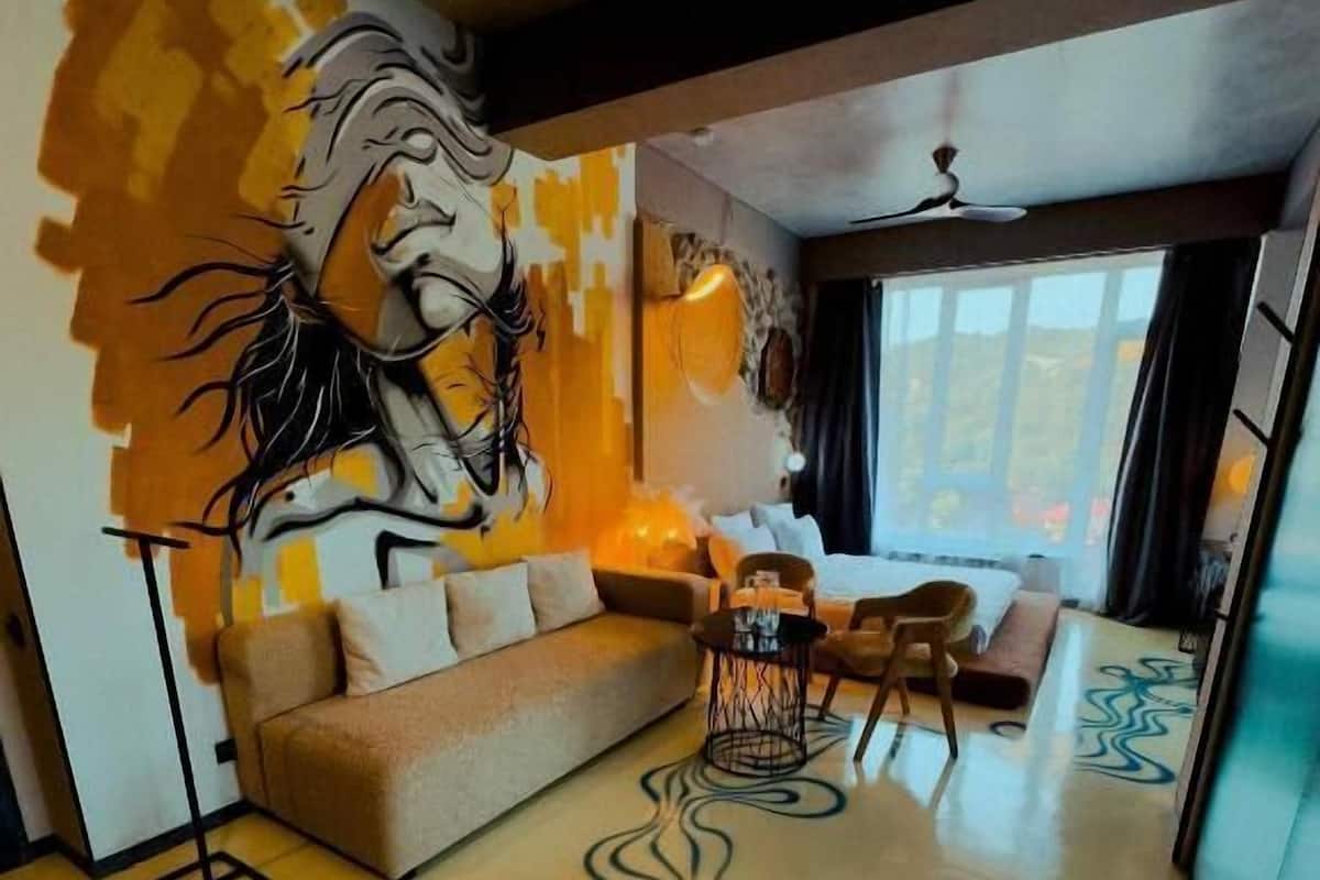 Un salon moderne avec un canapé, une table basse et des fauteuils. Un grand tableau abstrait orne le mur et un tapis à motifs recouvre le sol.