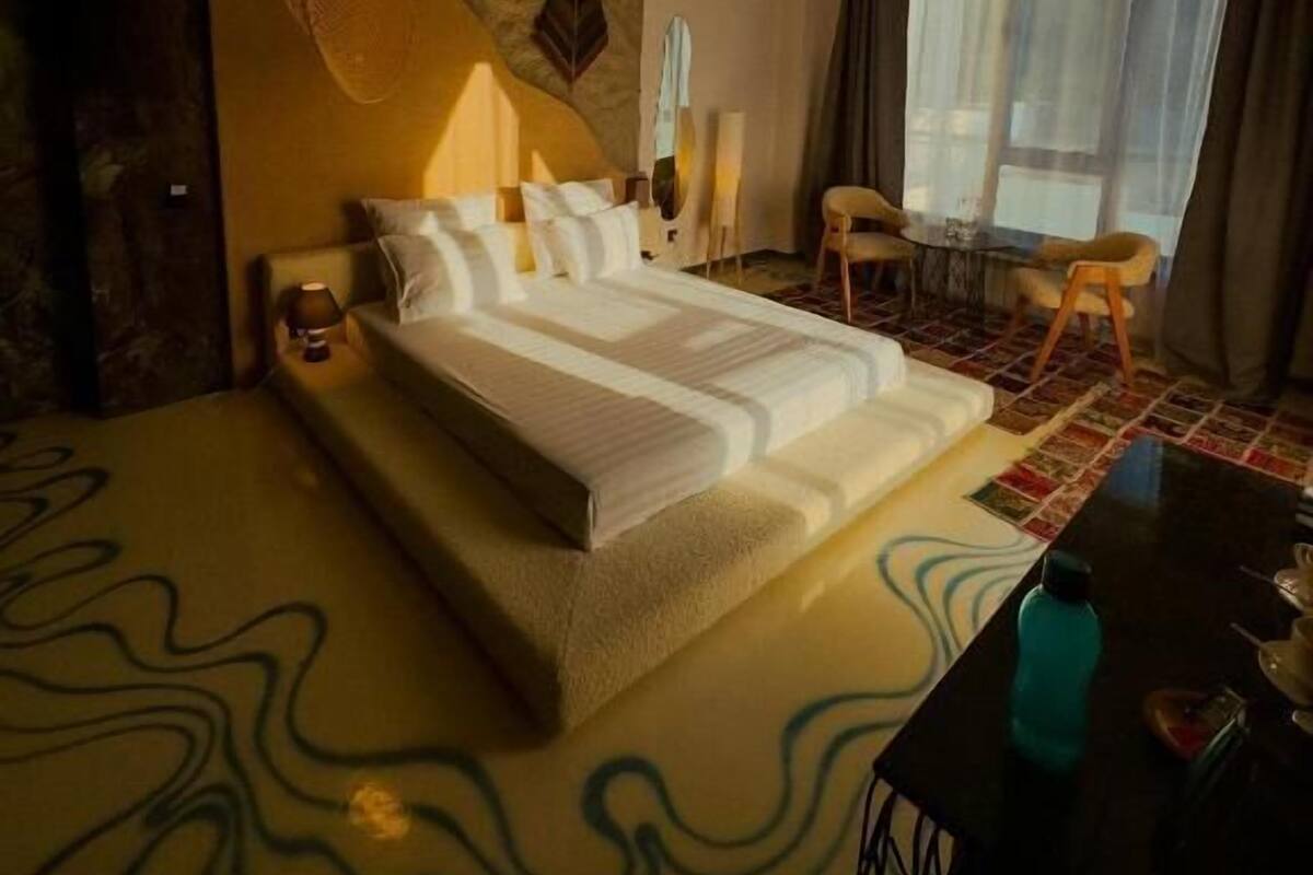 Une chambre d’hôtel avec un grand lit, un ventilateur de plafond, un bureau avec une chaise et une fenêtre avec des rideaux.