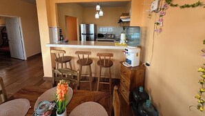 Una cocina con una isla central, taburetes de bar, dispensador de agua y refrigerador.