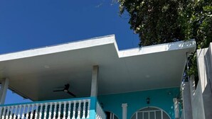 Un edificio de dos pisos con fachada azul, un balcón blanco y una escalera de hormigón.