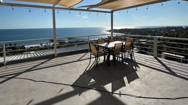 Un patio al aire libre con una mesa y sillas, vista al océano y cielo despejado.