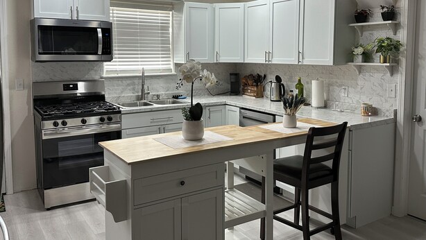 Een moderne keuken met witte kasten, een roestvrijstalen fornuis en een houten kookeiland met een stoel.