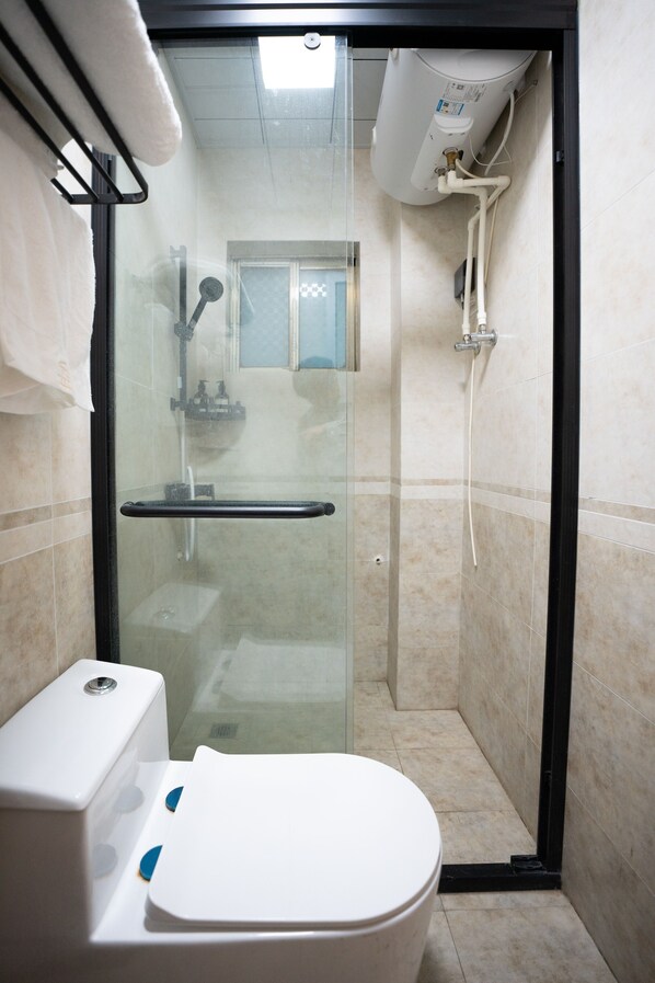 Un piccolo bagno privato con doccia, divisorio in vetro, water bianco e porta asciugamani.