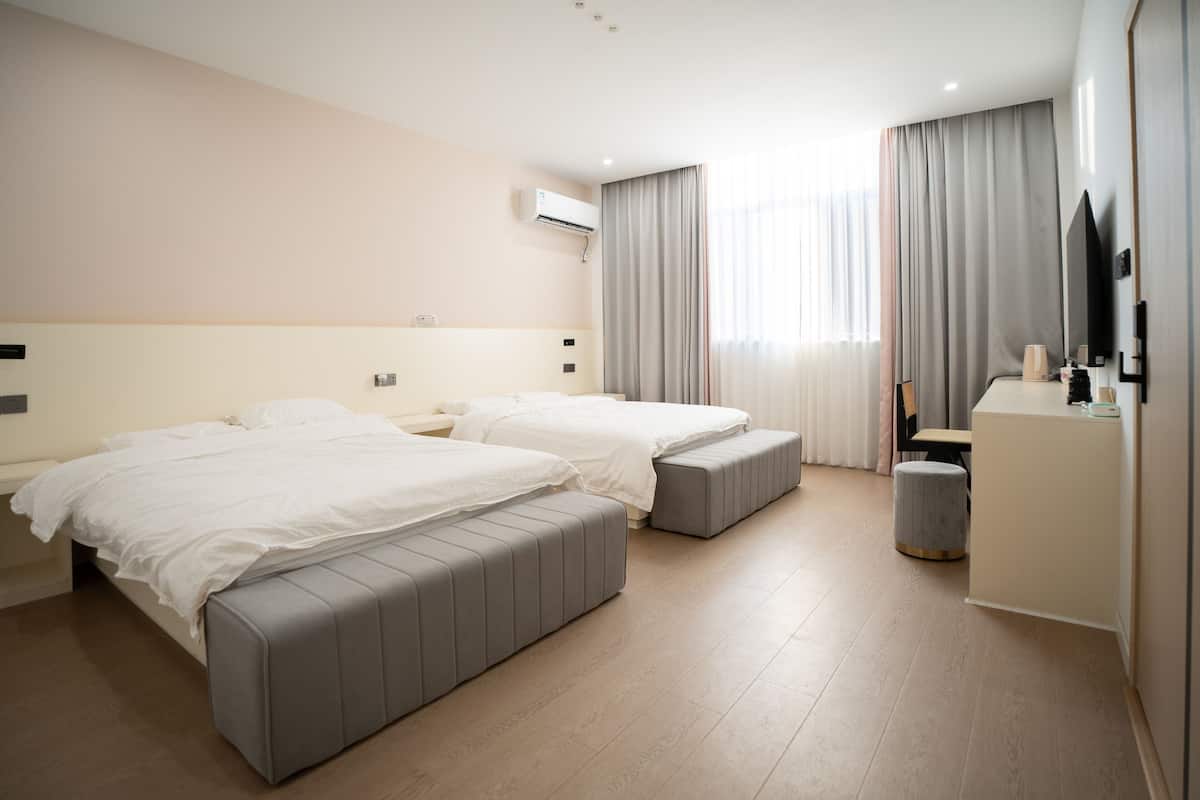 Habitación de hotel con dos camas, un escritorio, una silla, un equipo de aire acondicionado y un televisor.