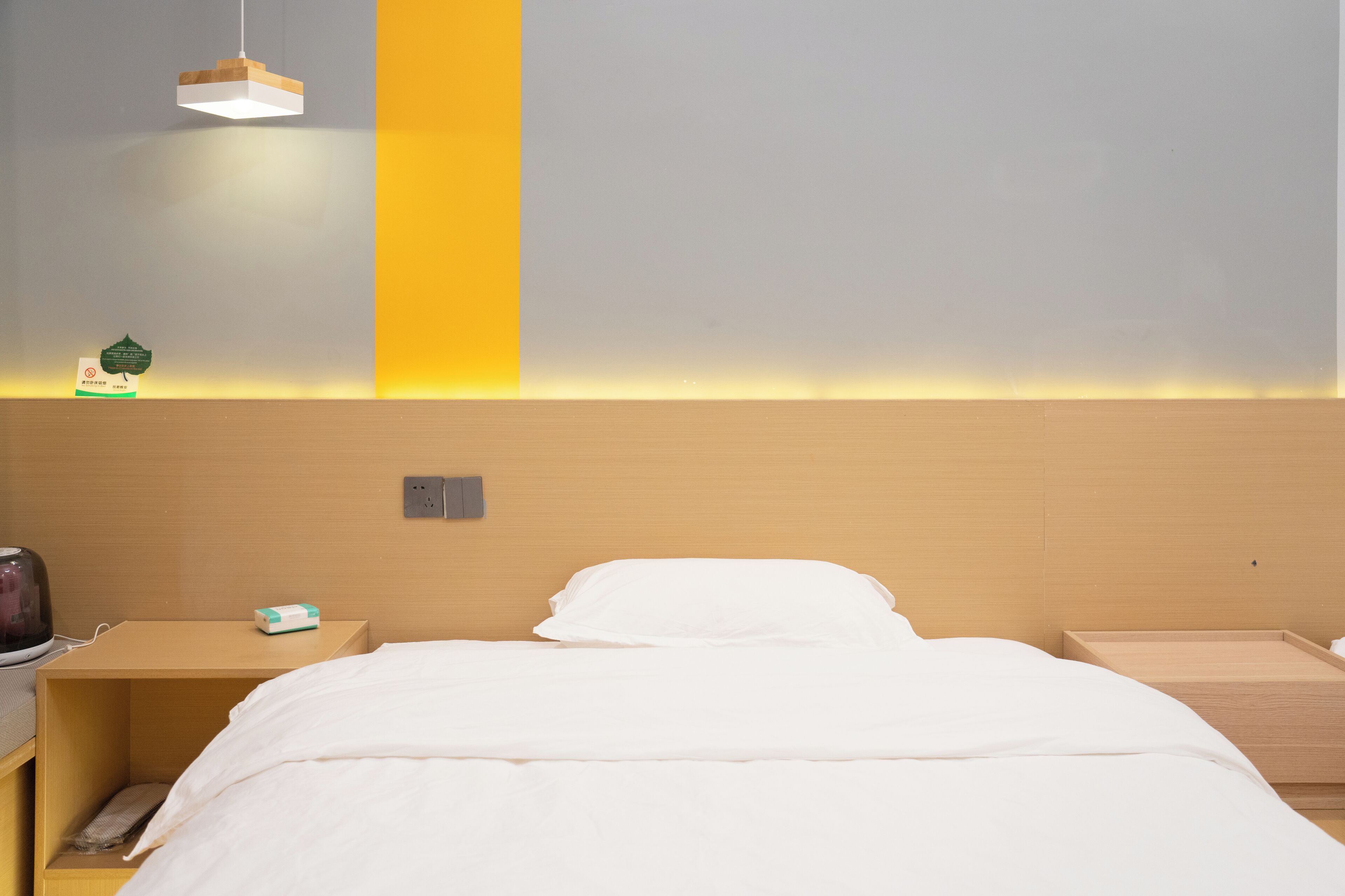 Et hotelværelse med en seng, sengeborde, en lampe og en vægmonteret hylde.