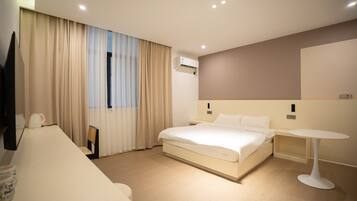 A modern hotel room with a large bed, bedside tables, a small round table, and an air conditioning unit.