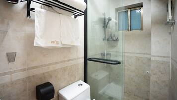 Un baño con cabina de ducha de vidrio, inodoro y toallero con dos toallas.