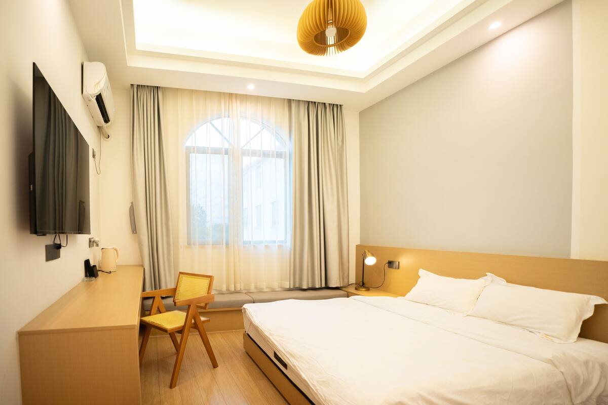 Una habitación de hotel con cama, escritorio, silla, televisor y ventana con cortinas.
