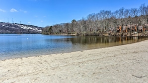A lakeside view with a sandy beach, a row of cabins, and a forested hillside. - Walk to Big Boulder Mtn & Lake, Home w/ Hot Tub! (Lake Harmony)