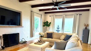 Ein geräumiges Wohnzimmer mit großem Flachbildfernseher, Kamin, einer Couch und Deckenventilator.