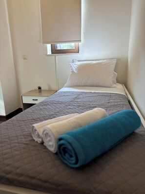 A neatly made bed with a quilted cover, a pillow, and rolled towels in white and blue. - Papyrise Oliveside (Heraklion)
