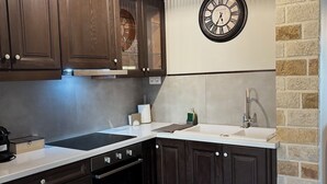 Uma cozinha com armários de madeira escura, bancada branca, forno embutido, pia e relógio fixado na parede.
