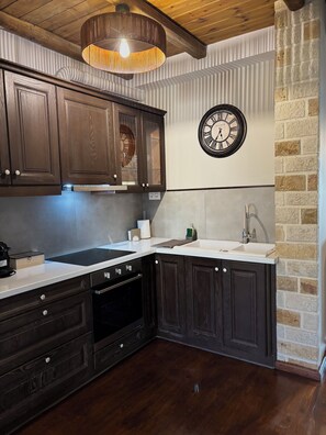 A kitchen with dark wooden cabinets, a white countertop, a built-in oven, a sink, and a wall-mounted clock. - Papyrise Oliveside (Heraklion)