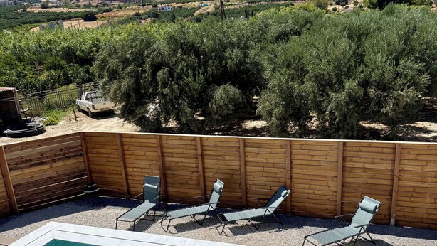 Una piscina rectangular con agua cristalina, rodeada por una valla de madera, y tres sillas de descanso.