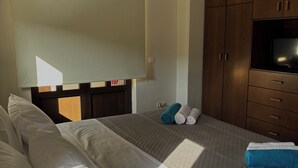 Quarto de hotel com cama, televisão, armários de madeira e janela.