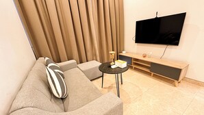 Una sala de estar moderna con un sofá gris, una mesita redonda, un televisor montado en la pared y un mueble bajo de madera.