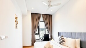 Un dormitorio moderno con una cama grande, ventilador de techo y vistas al exterior a través de una ventana con cortinas.