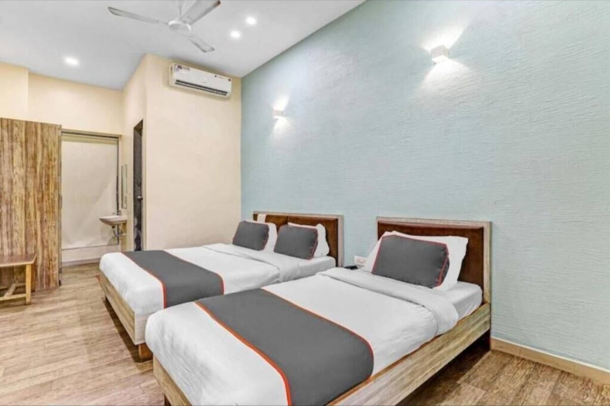 Een hotelkamer met twee bedden, een plafondventilator, een airconditioning en een houten bank.