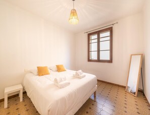 A bedroom with a bed, a small white nightstand, a window with a wooden frame, and a mirror on the wall. - Exceptional Villa Near the Alpilles (Graveson)