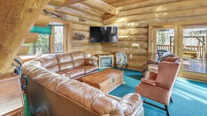 A log cabin interior with a large leather sectional sofa, a wooden coffee table, a television mounted on the wall, and a large window providing a view of the outdoors. - 5 Mi to Purgatory Resort, Mtn-View Family Cabin! (Durango)