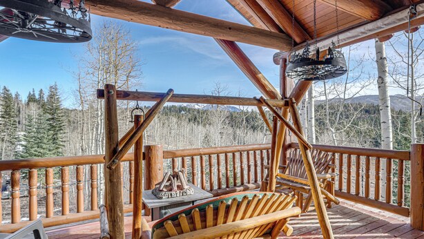 A wooden deck with a swing chair, a table with a fire pit, and a view of a forest and mountains. - 5 Mi to Purgatory Resort, Mtn-View Family Cabin! (Durango)