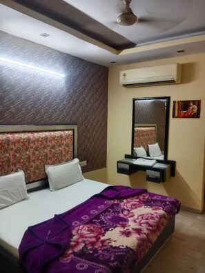 Een hotelkamer met een bed, nachtkastje, spiegel en een airconditioner.