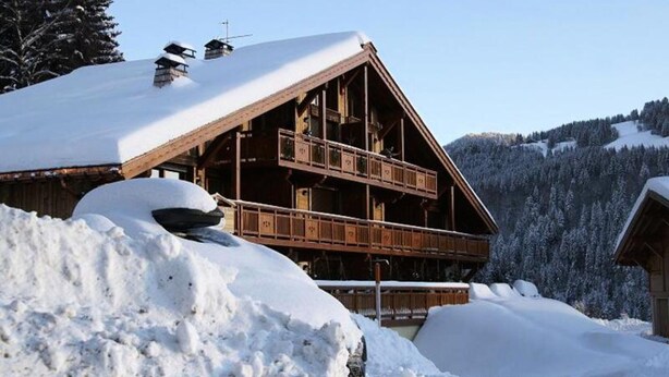 Una cabaña de madera con balcón, rodeada de montañas nevadas.