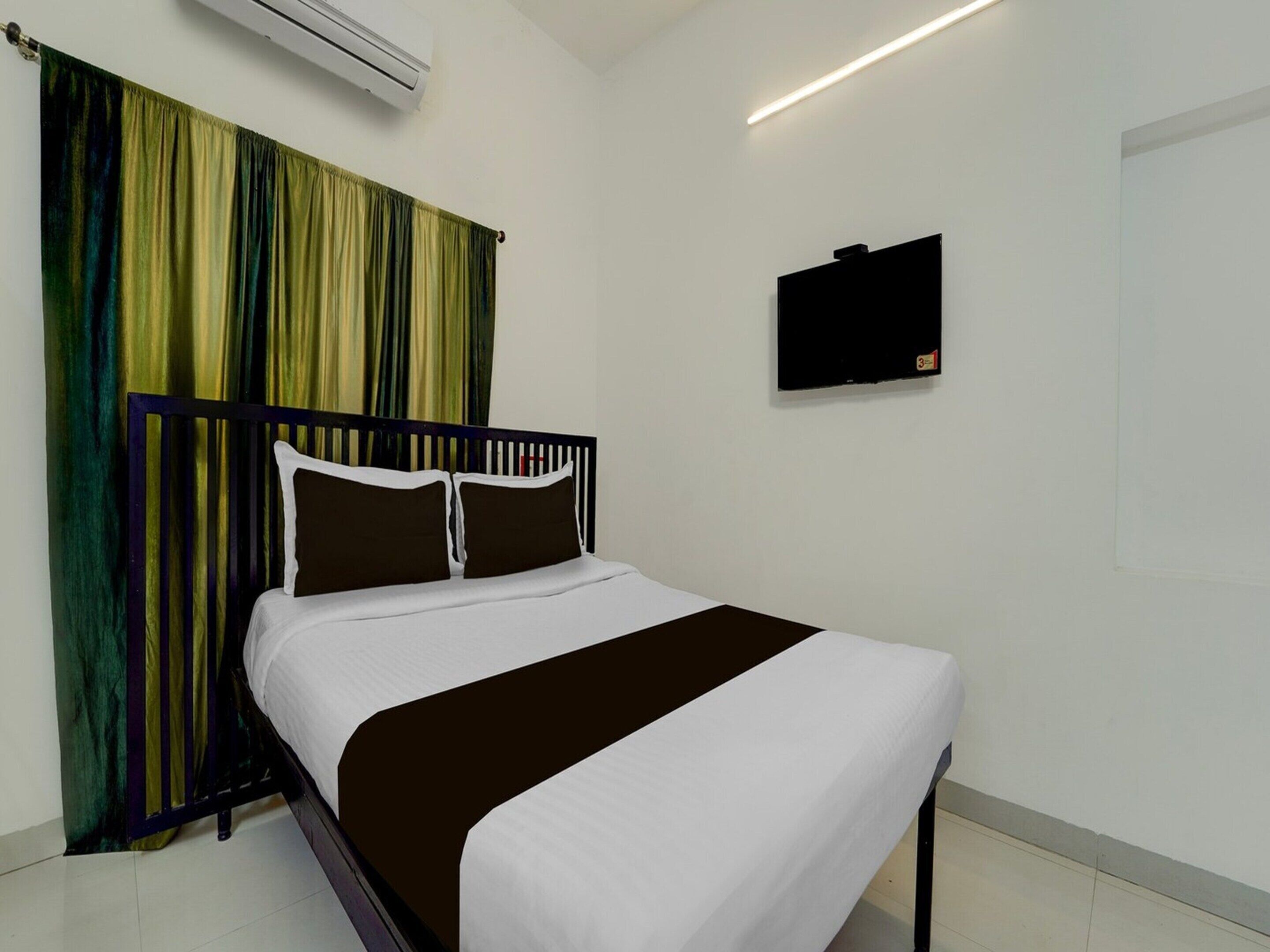 A hotel room with a bed, curtains, an air conditioner, a flat-screen TV, and a tiled floor.