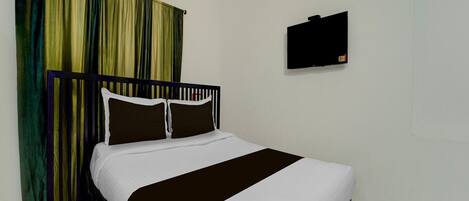 A hotel room with a bed, curtains, an air conditioner, a flat-screen TV, and a tiled floor.