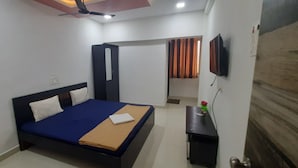A bedroom with a bed, a desk, a ceiling fan, and a door leading to another room. - Hotel Radhakrishna (Neral)