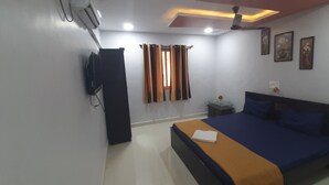 A bedroom with a bed, a TV, a ceiling fan, and a window with curtains. - Hotel Radhakrishna (Neral)