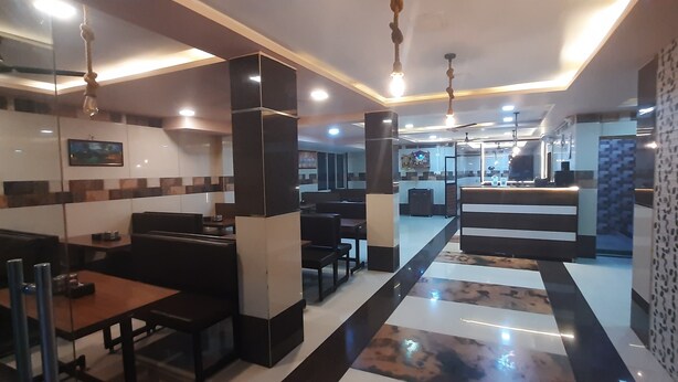 A modern restaurant with a central bar area, seating arrangements, and a patterned floor. - Hotel Radhakrishna (Neral)