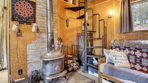 A cozy room with a wood-burning stove, a dartboard, and a bed with a motivational pillow. - Fire Pit & Water Views! Woodsy Tygh Valley Retreat (Tygh Valley)