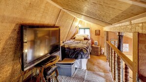 A cozy attic bedroom with a bed, a television, and a wooden staircase. - Fire Pit & Water Views! Woodsy Tygh Valley Retreat (Tygh Valley)