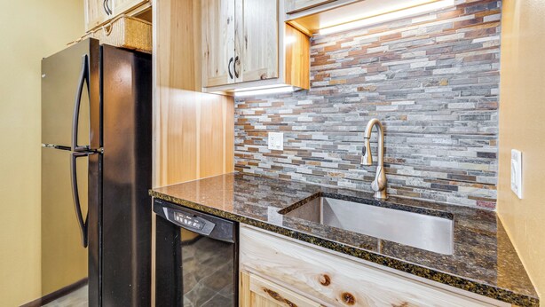 Eine Küche mit Holzschränken, einem Edelstahlkühlschrank, einer Granitabdeckung und einer Steinrückwand.