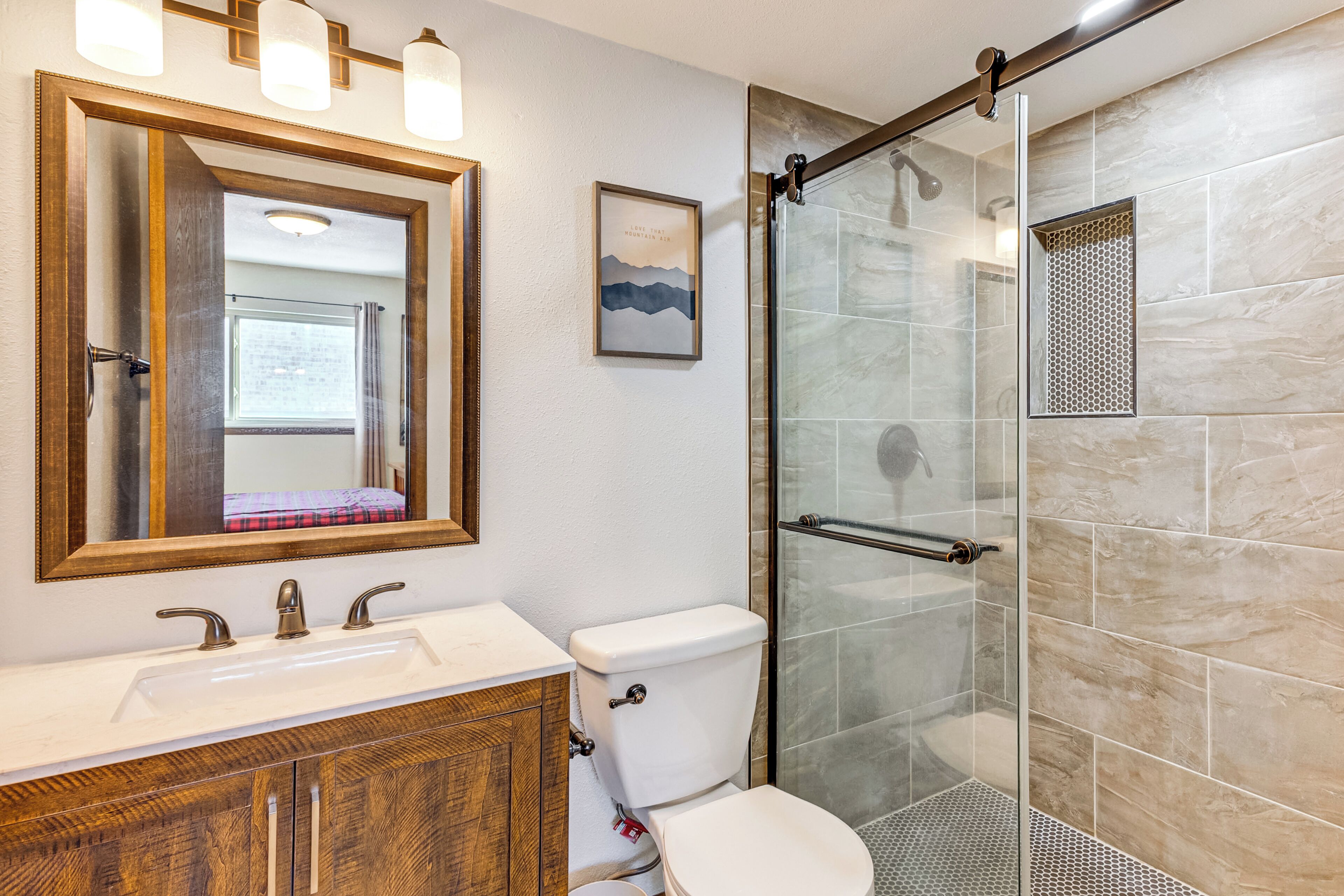 A bathroom with a wooden vanity, a white sink, a toilet, and a glass-enclosed shower.