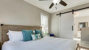 Une chambre à coucher avec un lit, un ventilateur de plafond, une fenêtre et une porte.