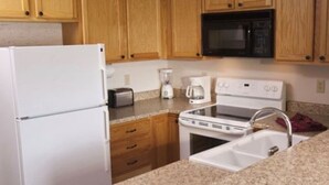 Una cocina con armarios de madera, un refrigerador blanco, un microondas, una estufa y un lavaplatos.