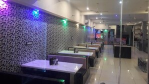 A restaurant with a patterned wall, multiple tables, and ceiling fans. - Gokul Hotel (Malpura)