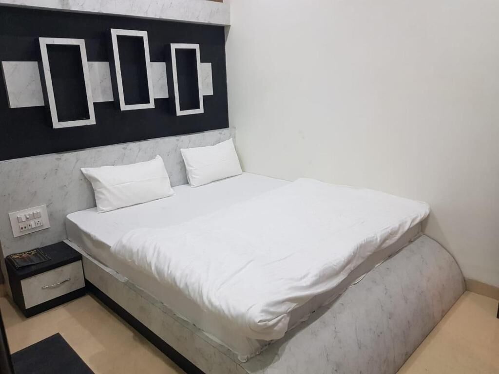 A bed with white bedding, a black headboard with geometric designs, a small bedside table, and a power outlet.