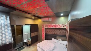 A bedroom with a round bed, a vanity with a mirror, a wardrobe, and a ceiling with a red abstract design. - Gokul Hotel (Malpura)