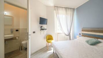 Quarto de hotel com cama, televisão, cadeira, banheiro com pia e janela com cortinas.