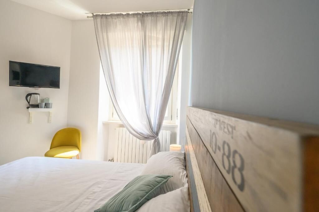 Una habitación de hotel con cama, televisor montado en la pared, una silla y una ventana con cortinas.