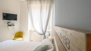 Una habitación de hotel con cama, televisor montado en la pared, una silla y una ventana con cortinas.