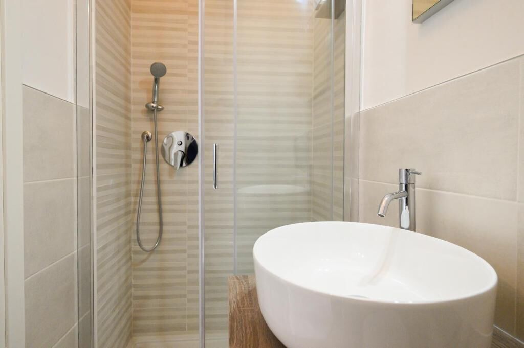 Ein modernes Badezimmer mit einer gläsernen Duschkabine, einem weißen Waschbecken und einem Spiegel darüber.