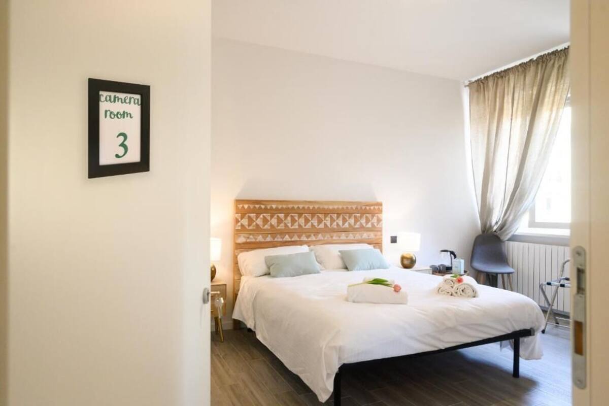 Une chambre à coucher bien rangée, avec un lit, une table de chevet, une lampe et un panneau indiquant qu’il s’agit d’une salle de prise de vue.