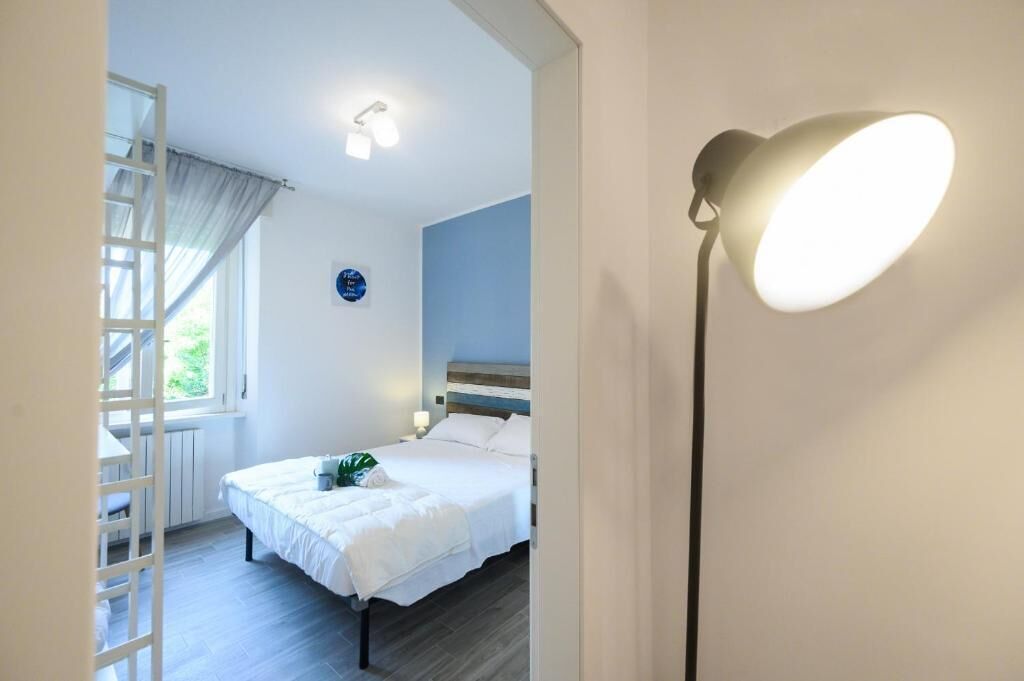 Un dormitorio con cama, mesita de noche, lámpara, ventana con cortinas y vistas al exterior.