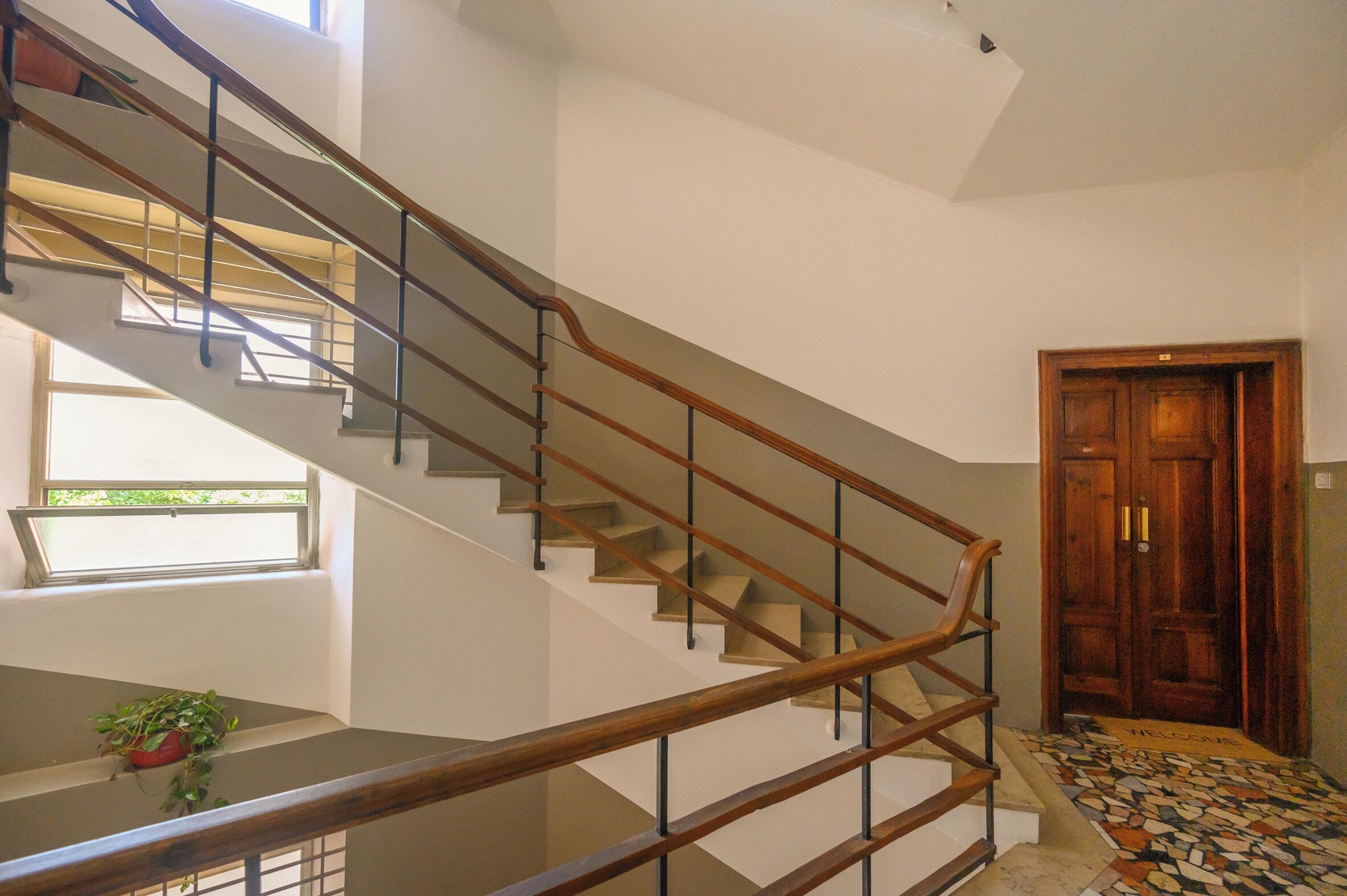 Una escalera con barandillas de madera y una baranda de metal, que conduce a un rellano con una planta en maceta.